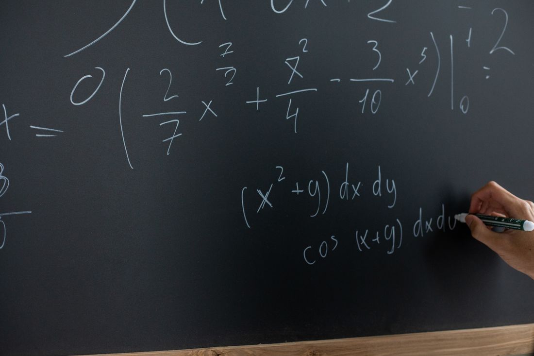 A hand writing equations on a dark chalkboard