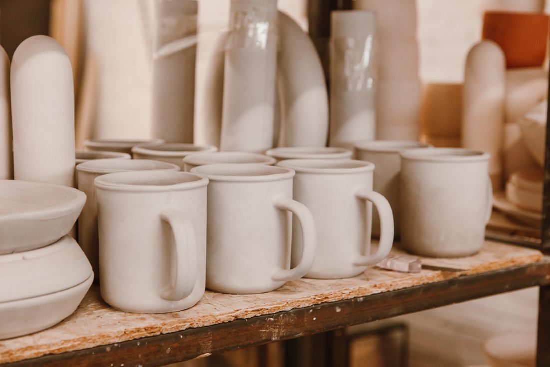 Unfinished ceramic mugs on a workshop shelf awaiting glazing